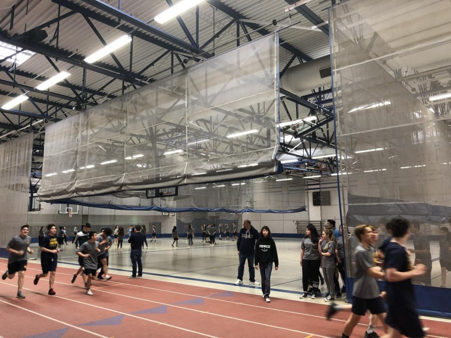 PE students running laps in the fieldhouse and begin to stretch in preparation for a day of challenging fitness ahead.