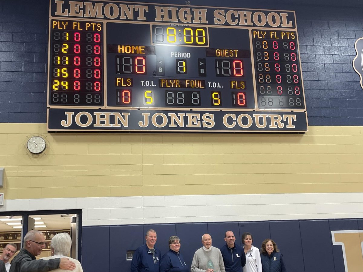 Members of the District 210 Board of Education standing under the scoreboard with Coach Jones. Pictured from left to right: board members Mike Kardas, Pam Driscoll, honoree John Jones, Kurt Korte, Lynn Antonopoulos and Beverly Marzec.